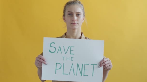 Retrato de una activista seria sosteniendo la pancarta de Save Planet sobre fondo amarillo — Vídeo de stock