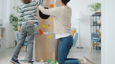 Anne ve oğlunun evde çıkartmalarla karton uzay gemisi dekorasyonu yapmaları yavaş bir hareket.