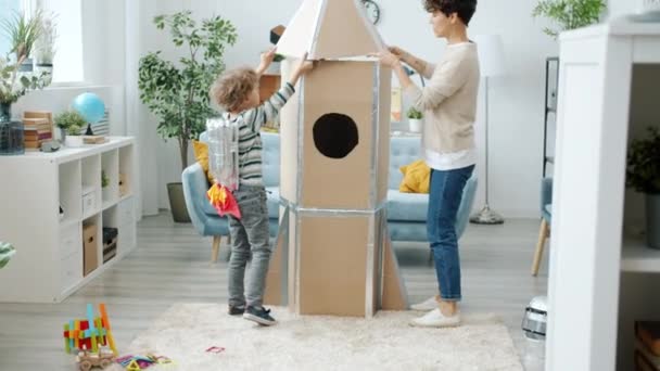 Gelukkig familie moeder en zoon maken kartonnen raket spelen samen in appartement — Stockvideo