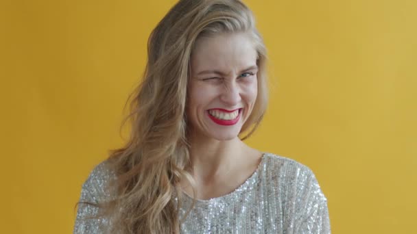 Retrato de câmera lenta de menina atraente soprando brilhos de prata e rindo no fundo amarelo — Vídeo de Stock