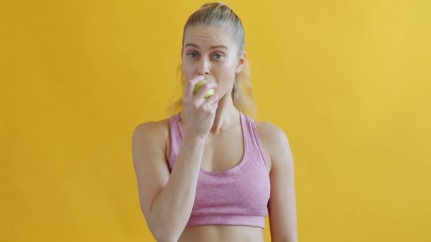 Linda deportista comiendo manzana disfrutando de fruta fresca sobre fondo amarillo — Vídeos de Stock