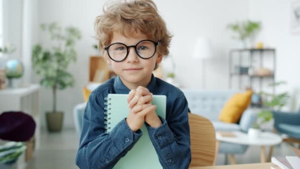 Αργή κίνηση πορτρέτο του αξιολάτρευτο παιδί φορώντας γυαλιά κρατώντας βιβλίο χαμογελώντας στο διαμέρισμα — Αρχείο Βίντεο