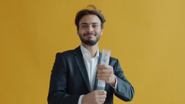 Медленный портрет ближневосточного мужчины, бросающего конфетти смеясь и танцуя на жёлтом фоне — стоковое видео