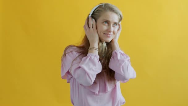 Ritratto di ragazza felice che ascolta musica attraverso le cuffie e canta su sfondo giallo — Video Stock