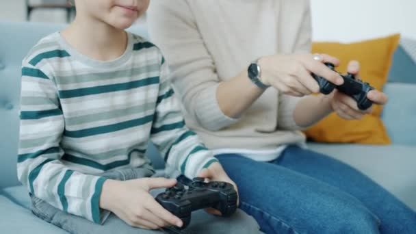 Мати і син грають у відеогру з джойстиками, сміючись над п'ятьма вдома — стокове відео