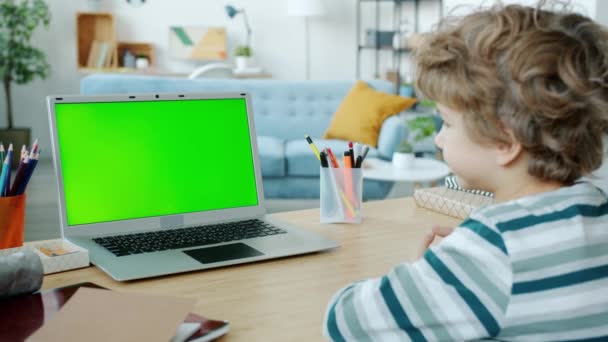 Ragazzino serio che studia online guardando il computer portatile chiave chroma schermo verde in appartamento — Video Stock