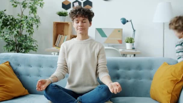 Genç bir kadın Lotus pozisyonunda meditasyon yaparken hiperaktif bir çocuk evde çığlık çığlığa koşuyor. — Stok video