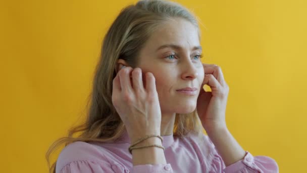 Retrato de chica moderna usando auriculares y bailando escuchando música sobre fondo amarillo — Vídeo de stock