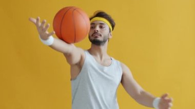 Yakışıklı Arap sporcu basketbolla oynuyor ve kameraya bakıyor.