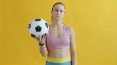 Elinde futbol topu olan ve kameraya kırmızı kart gösteren genç bir kadının portresi.