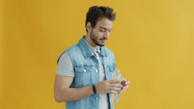 Su içen ve sarı arka plandaki kameraya bakan genç bir Arap 'ın yavaş çekim portresi.