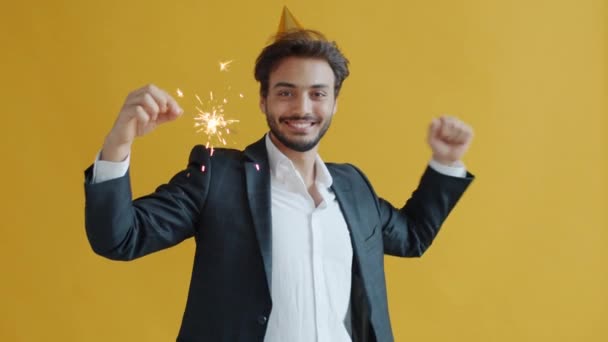 Slow motion portrait of merry Middle Eastern man dancing holding bengal light wearing birthday hat — Stock Video