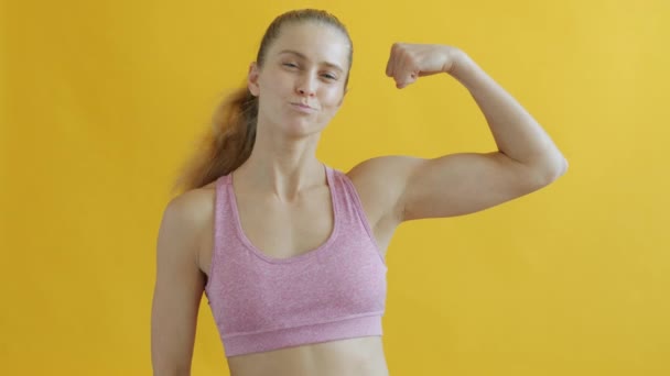 Портрет мускулистой молодой спортсменки, показывающей бицепсы и улыбающейся, глядя в камеру — стоковое видео