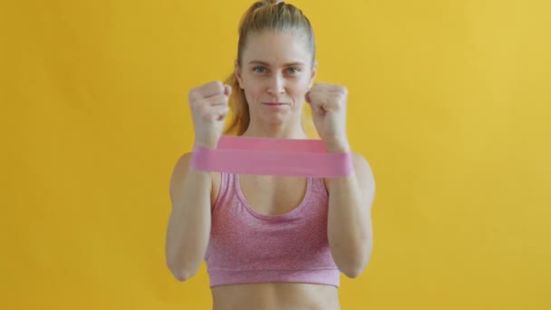 Langzame beweging van jonge vrouw die sportbeha draagt en traint met fitness weerstandsband — Stockvideo