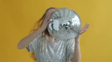 Disko topu tutan güzel bir kadının portresi. Sarı arka planda güneş gözlüğü takıyor.