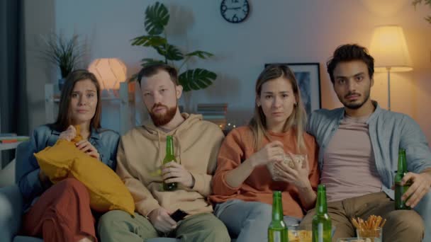 多文化朋友小组在电视上看恐怖片，吃爆米花，在黑暗的房子里喝啤酒 — 图库视频影像