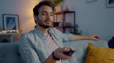 Akşamları elinde uzaktan kumandayla televizyon izleyen yakışıklı genç adamın portresi.