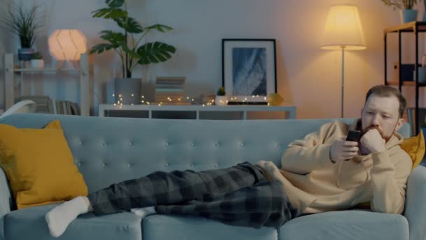 Πορτρέτο του όμορφου άνδρα που ανοίγει την τηλεόραση κάθεται στον καναπέ στο διαμέρισμα βλέποντας έκτακτη είδηση το βράδυ — Αρχείο Βίντεο