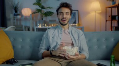 Neşeli Orta Doğulu birinin portresi TV 'de film izlerken gülerken ve evde patlamış mısır yerken.