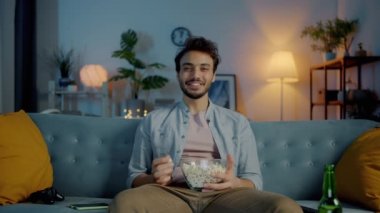 Çekici bir esmerin portresi patlamış mısır yiyor ve karanlık evde televizyon izlerken gülüyor. Boş zaman aktivitesi ve eğlence konsepti.
