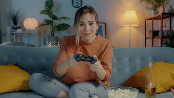 Портрет веселой молодой женщины, развлекающейся с видеоигрой, играющей в одиночку, смотрящей в камеру ночью — стоковое видео
