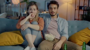 Karanlık evde kanepede oturmuş elinde patlamış mısırla korku filmi izleyen kadın ve erkeğin portresi. Duygu ve eğlence konsepti.