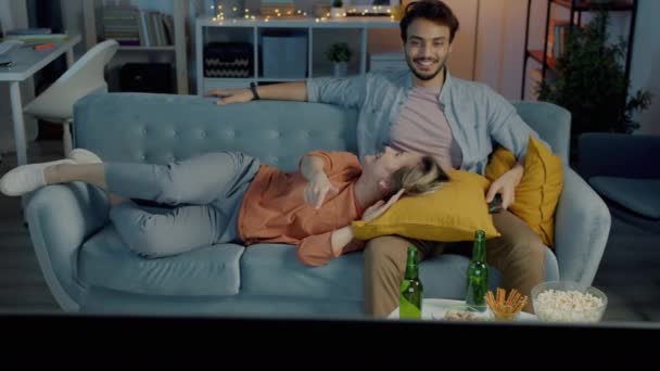 暗いリビングルームで一緒に夜を楽しむソファの上に寝そべって夜にテレビを見て幸せな家族 関係と国内生活の概念 — ストック動画