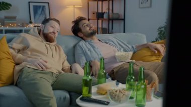 Sarhoş öğrenciler kirli kanepede uzanmış patlamış mısır atıyor ve akşamları evde televizyon izliyorlar.