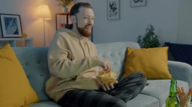 Mutlu genç bir adamın portresi TV izliyor cips yiyor ve akşam evde bira içiyor..
