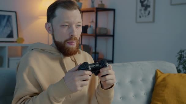 Портрет эмоционального человека с удовольствием играющего в видеоигры жестом и улыбающегося в темном доме — стоковое видео