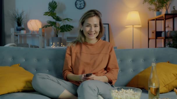 Portrait of pretty lady watching interesting movie on TV sitting on couch in dark house and looking at camera — Stock Video