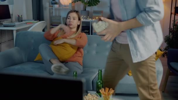 Retrato del marido y la esposa sentados en el sofá en casa viendo la televisión y comiendo palomitas de maíz por la noche — Vídeos de Stock