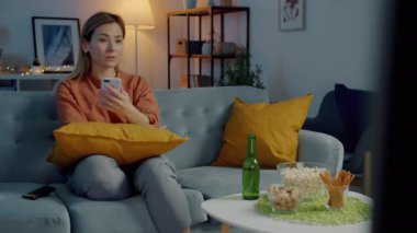 Akıllı telefon kullanan, ekrana dokunan ve akşam evde televizyon izleyen çekici melez kadın.