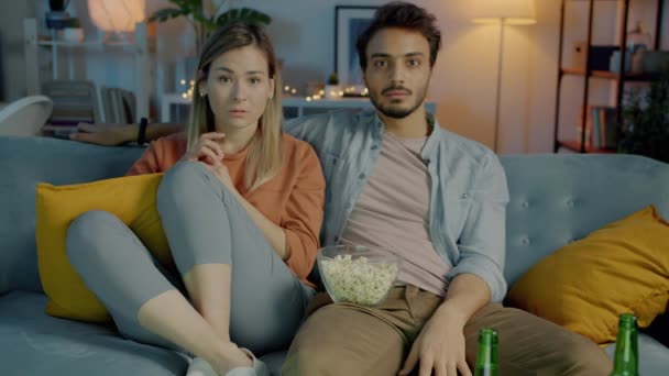Портрет двох людей пара дивиться страшний фільм по телевізору обіймає попкорн в темній квартирі — стокове відео