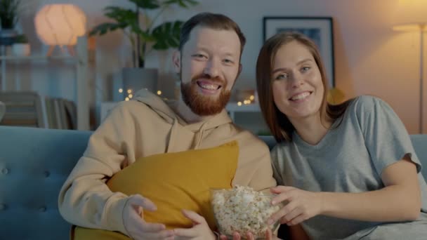 Весела молода пара дивиться телевізор сміється весело насолоджуючись ніччю в квартирі — стокове відео
