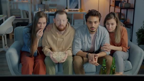 Grupp studenter tittar thriller på TV hemma på kvällen och känner sig rädda stirrar på skärmen äta popcorn — Stockvideo