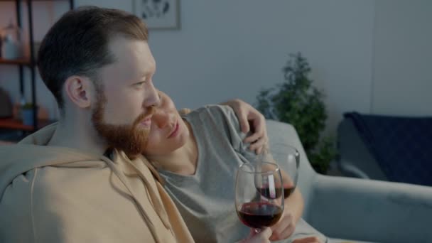Junger Mann schaut mit Freundin fern, trinkt Rotwein und redet im dunklen Haus auf Couch — Stockvideo