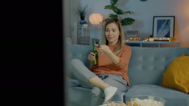 Güzel melez kadın televizyon seyrediyor. Koyu bir dairede şişeden gülüyor ve içiyor.