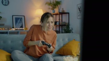 Video oyunu oynayan duygusal melez kadın portresi. Koyu renkli bir dairede, koltukta oturarak oyun kaybediyor.