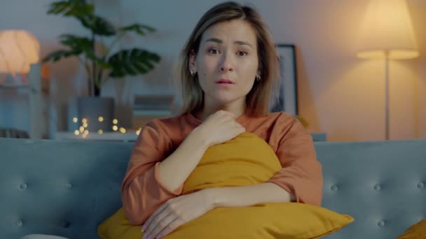 Retrato de una jovencita viendo noticias de última hora en la televisión y llorando sentada en un sofá en un cuarto oscuro — Vídeo de stock