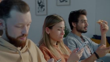 Akıllı telefonları kullanan, pizza yiyen ve geceleri karanlık oturma odasında televizyon izleyen bir grup genç.