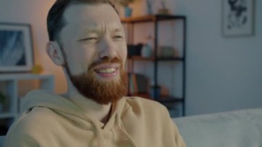 Neşeli adam TV 'de komik film izlerken güler ve şişeden bira içerken gece evde eğlenir.