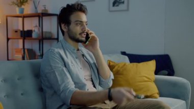 Ortadoğulu öğrenci cep telefonuyla sohbet ediyor ve geceleri aydınlık evde televizyon seyrediyor.