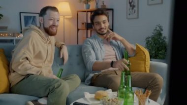Neşeli erkek arkadaşlar televizyon izleyip bira içerek akşam yemeğinin tadını çıkarıyorlar.