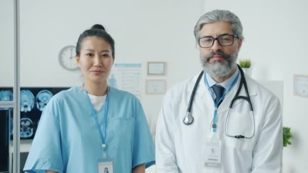 Portrait of male physician in white gown and female nurse in scrubs standing in clinic office — Stock Video
