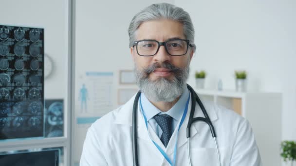 Retrato en cámara lenta del doctor hombre maduro sonriendo y mirando a la cámara en la oficina moderna — Vídeos de Stock