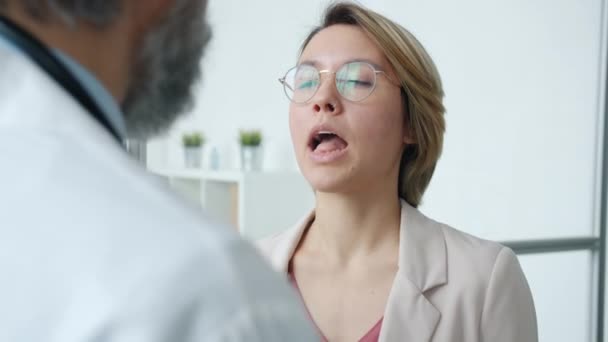 Mujer joven que abre la boca mostrando la garganta durante el examen médico con el médico masculino — Vídeos de Stock
