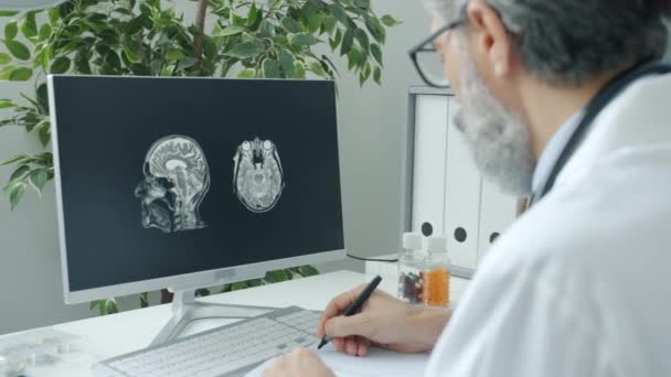 Mature doctor working with computer analyzing brain scan on screen indoors in hospital office — Stock Video