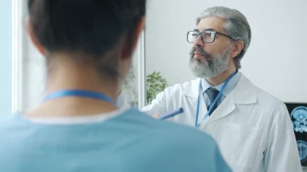 Neurologista analisando exames cerebrais discutindo imagens de RM com enfermeira no quarto do hospital — Vídeo de Stock