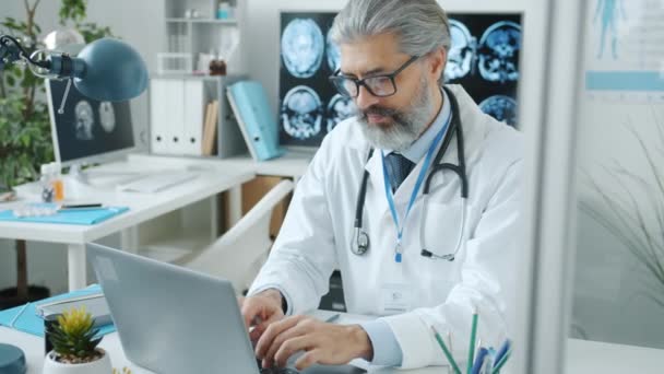 有经验的医生穿着白色长袍，用笔记本电脑打字，专注于日常工作 — 图库视频影像